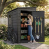 Woman arranging garden gear in a resin vertical tool shed with yard tools hanging on the door and a bicycle parked nearby.