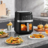 Sejoy air fryer on marble kitchen counter with roasted chicken visible through window, surrounded by fried chicken, sliders, and vegetables